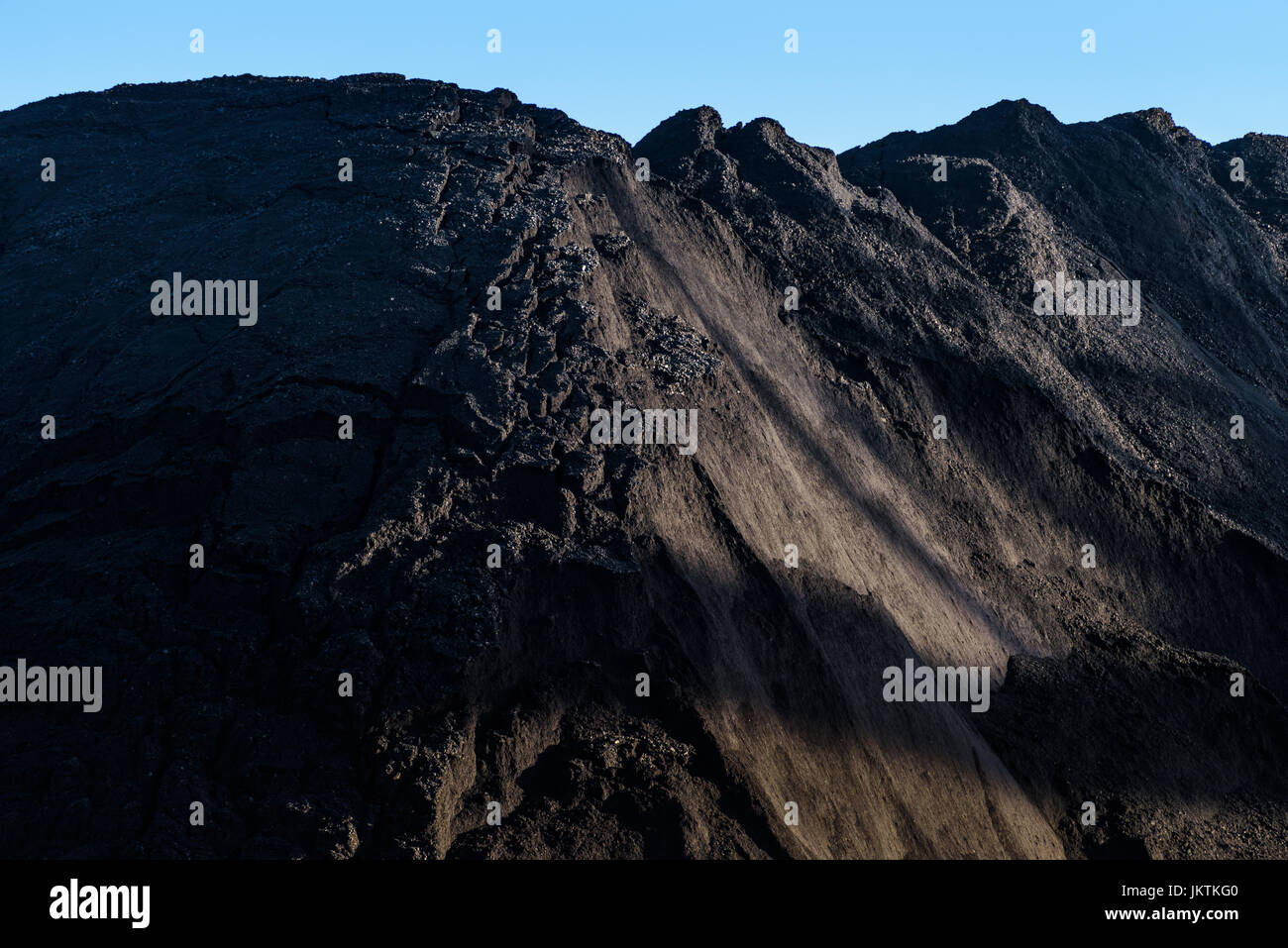 Un grande mucchio di carbone che giace nella parte bassa della luce solare con un cielo blu sopra. Foto Stock