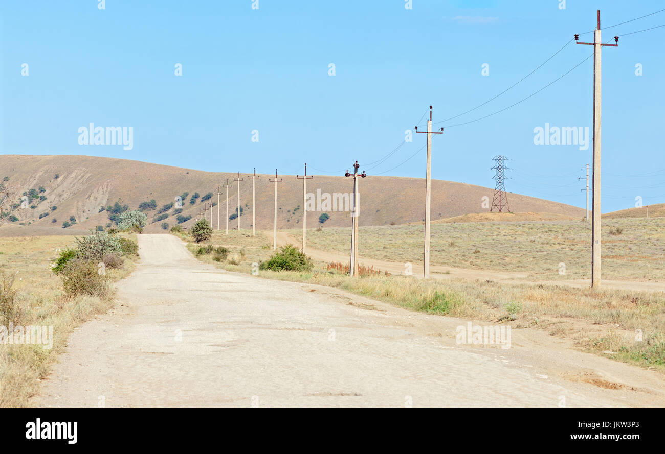 La vecchia strada nella regione arida con pali di calcestruzzo per l'energia elettrica lungo il cordolo. Penisola di Crimea Foto Stock