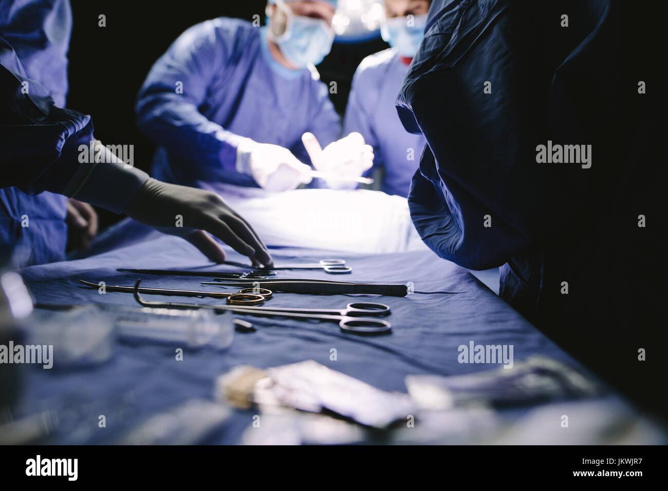 Close-up di infermiere prendendo gli strumenti medici per il funzionamento con i colleghi di fare un intervento chirurgico in background. Il team medico di eseguire l'operazione in ospedale. Foto Stock