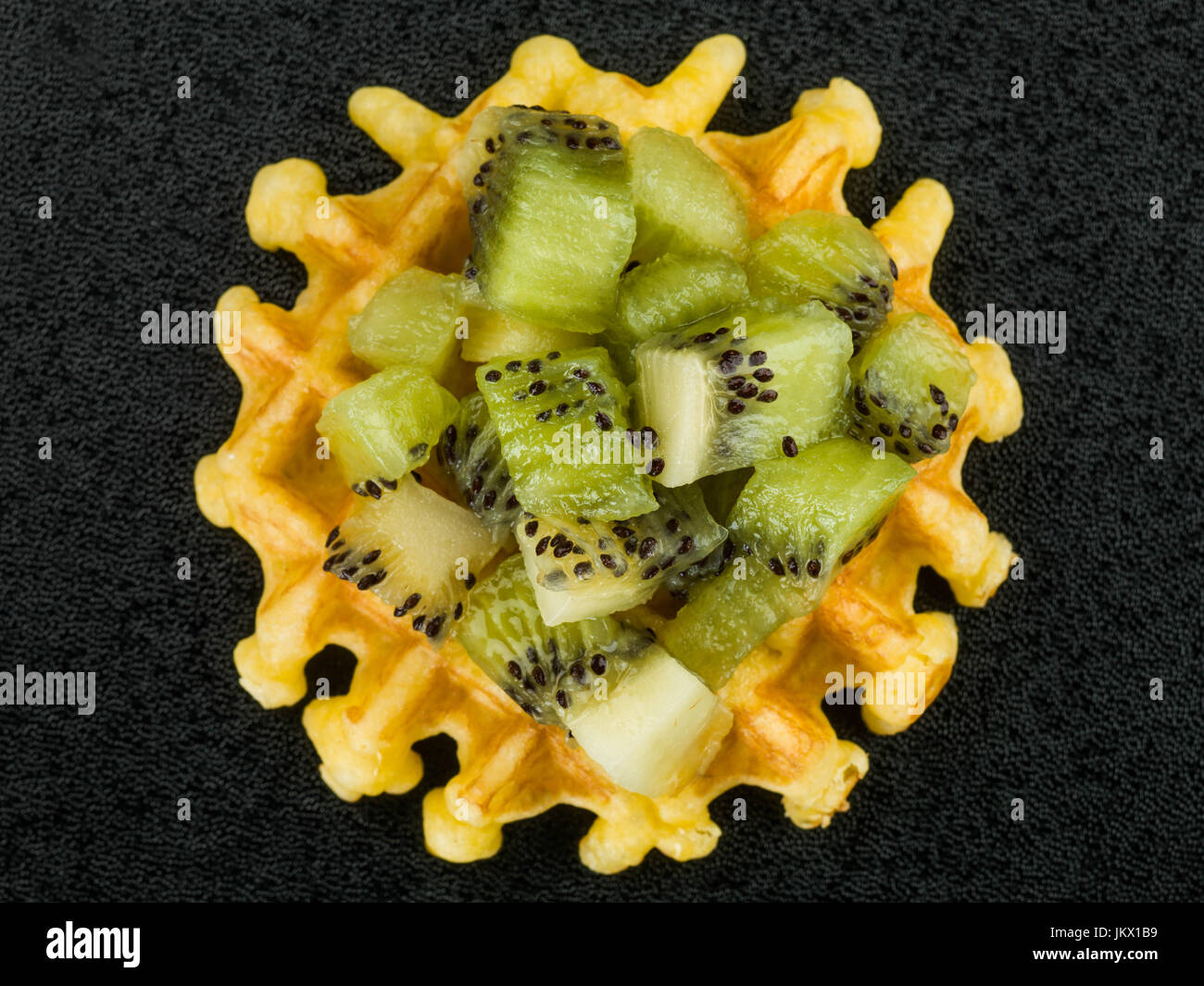 Solo il burro belga waffle e rabboccato con fresche kiwi contro uno sfondo nero Foto Stock