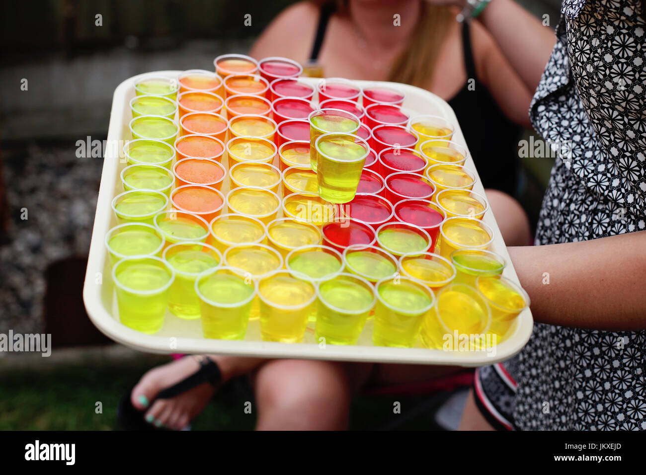 Una persona che porta un vassoio di colorati scatti di alcool Foto Stock