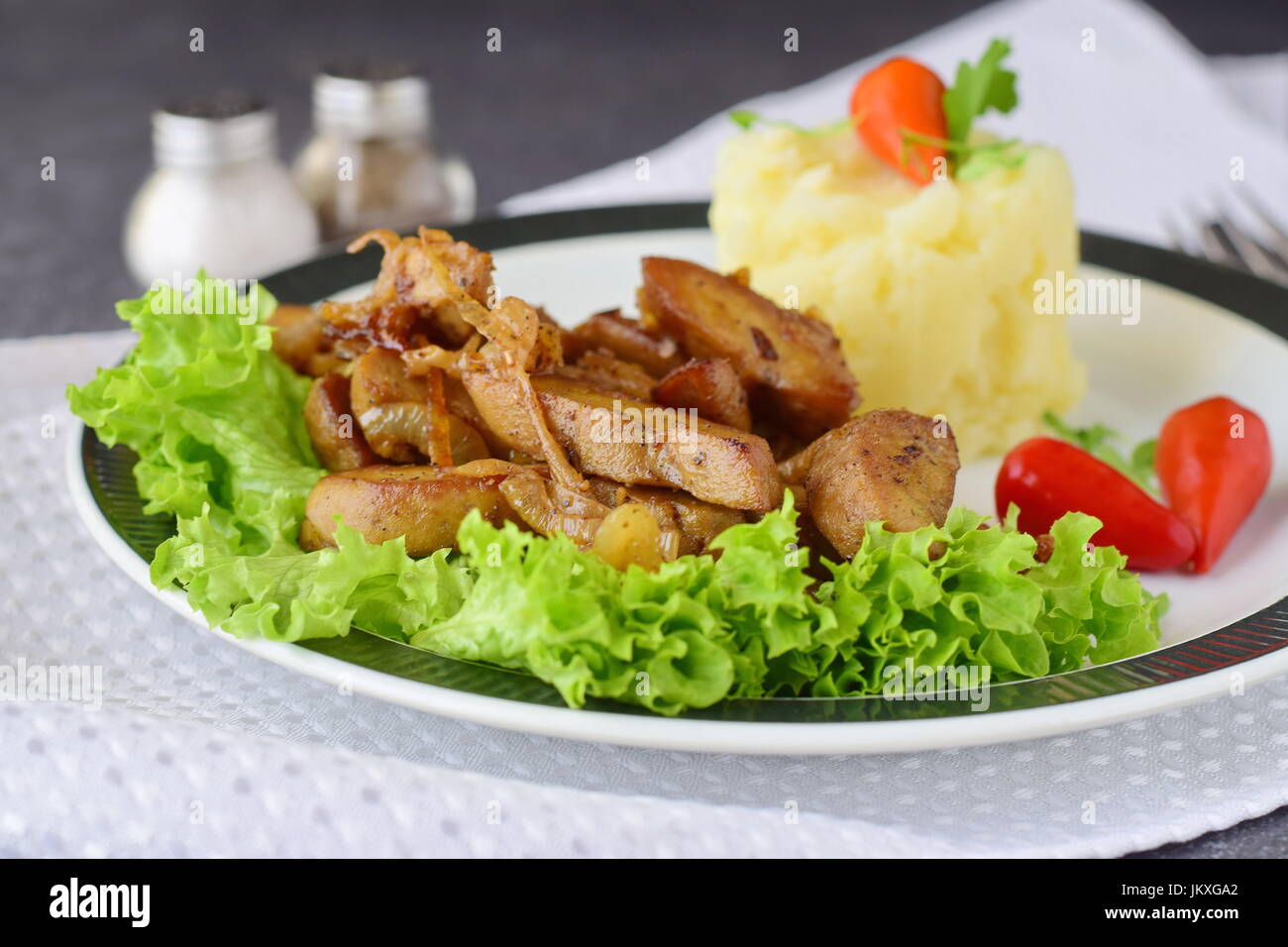 Fried bull testicoli con crema di erbe e servita con purea di patate su una piastra bianca su un sfondo astratto. Cibo sano concetto. Foto Stock