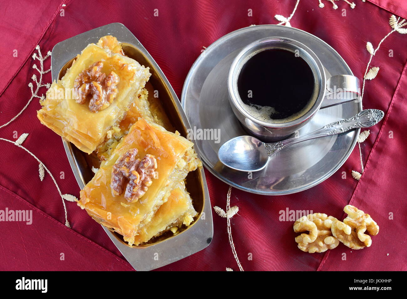 Tradizionale greco per il baklava realizzata con filo di impasto, lo sciroppo di zucchero e wallnuts su un vassoio di metallo con metallo tazza da caffè su un panno viola sfondo. Foto Stock