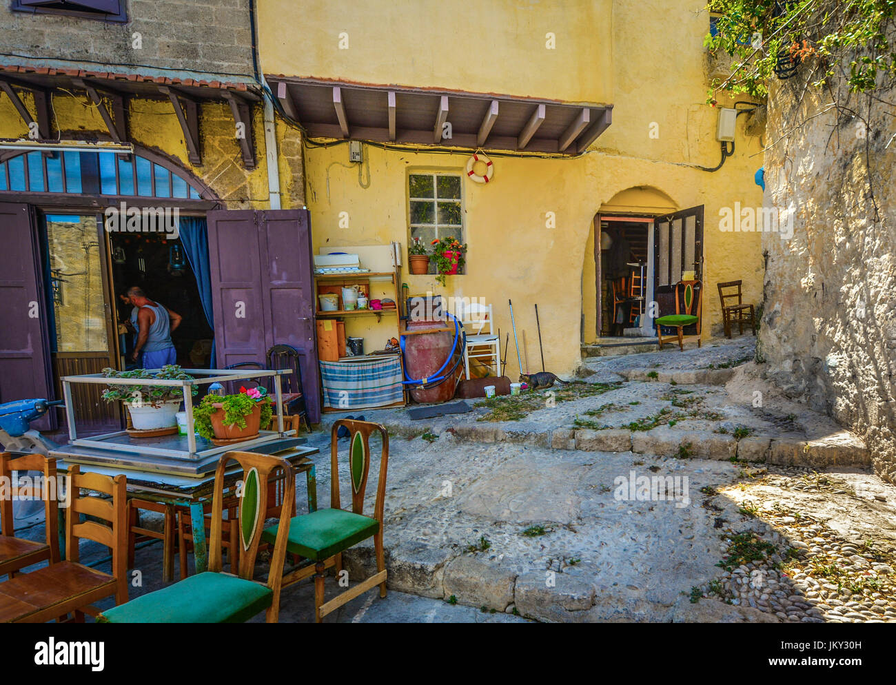 Al di fuori della modalità cafe apertura per business sull'isola Mediterranea di Rodi Grecia. Un gatto caccia e stocchi un piccione al di fuori della porta. Foto Stock