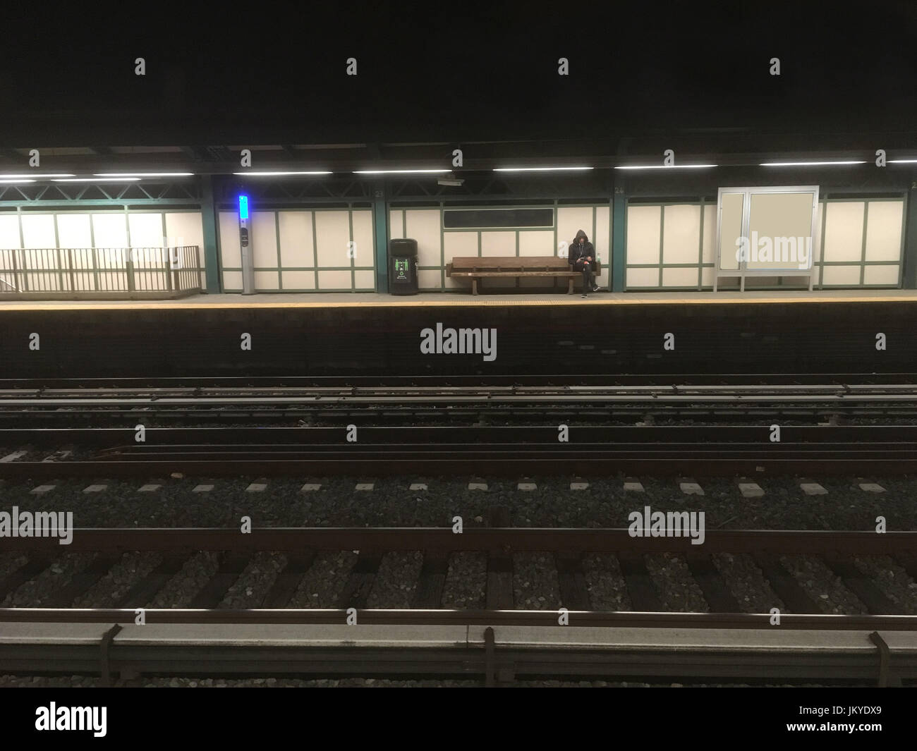 Uomo seduto su una panca di legno in attesa per la metropolitana in ritardo una notte di t. L'uomo attende il treno. New York City i mezzi di trasporto pubblici. Attesa per la metropolitana. Foto Stock
