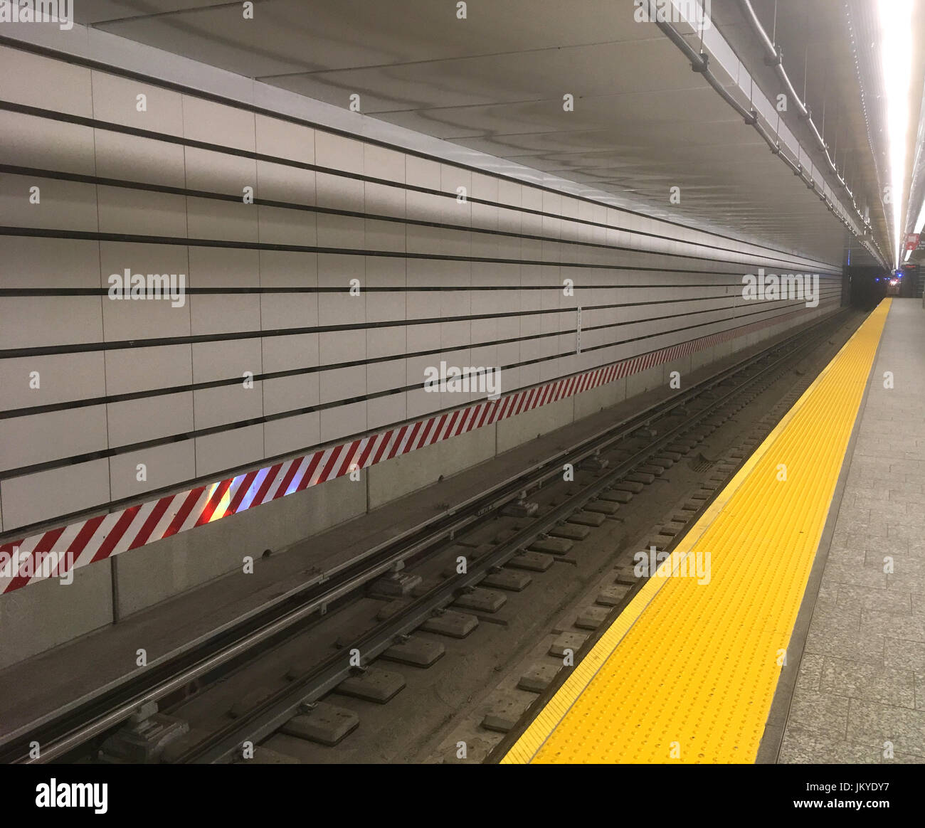 Guardando lungo le piste del treno dalla piattaforma in una stazione della metropolitana di New York City. Piastrelle bianche della metropolitana e una linea gialla dipinta sulla piattaforma a New York. Foto Stock