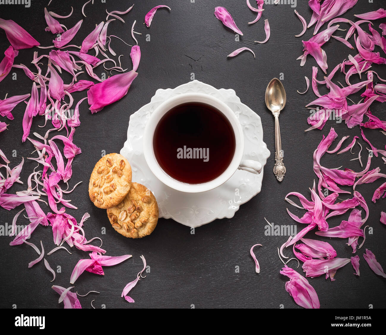 Nero caffè in tazza con due biscotti e peonia petali sparsi intorno Foto Stock