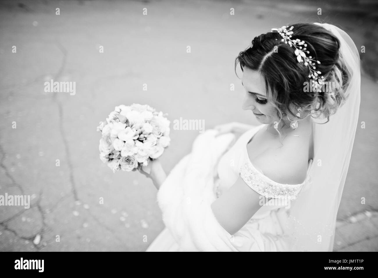 Close-up verticale di una bella sposa tenendo un mazzo di fiori e in posa sulla strada. Foto in bianco e nero. Foto Stock