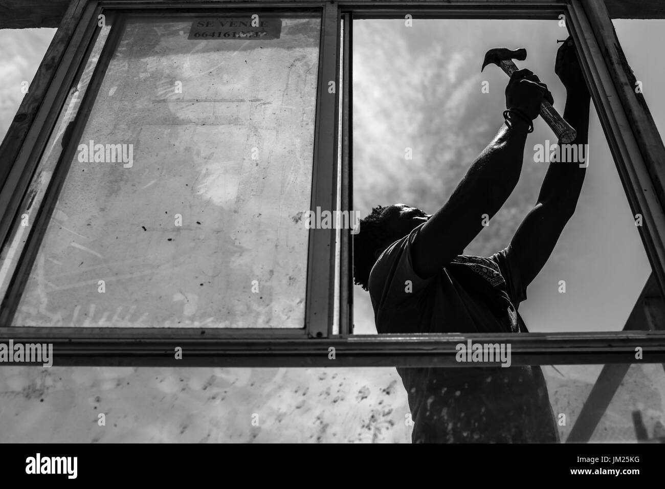 Tijuana, Baja California, Messico. 19 Luglio, 2017. Un emigrante haitiano installa una finestra di una struttura lungo un acqua secca canal si trova nella periferia di Tijuana, Baja California. Durante la stagione delle piogge, il canale viene contaminato con cestino e liquami provenienti dalla vicina discarica. Il governo locale ha rifiutato di concedere i permessi di costruzione per la chiesa principale di ricovero di immigrati haitiani nella zona sostenendo che esso si trova in una zona di rischio. Tuttavia, il pastore della chiesa ha deciso di andare avanti con la costruzione di case per i migranti prendendo atto che la situazione è una crisi umanitaria Foto Stock