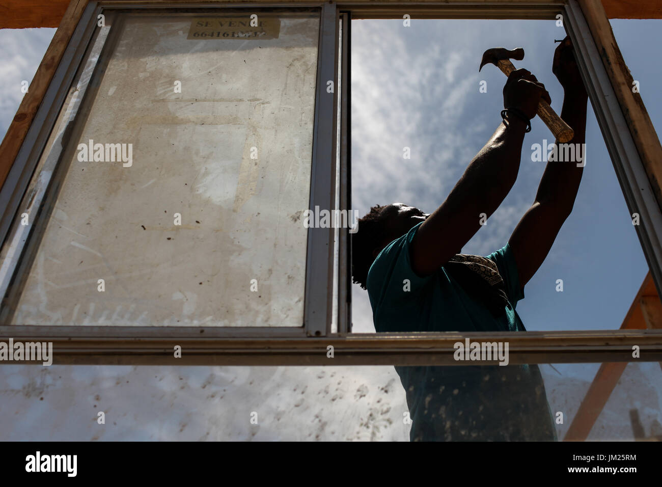 Tijuana, Baja California, Messico. 19 Luglio, 2017. Un emigrante haitiano installa una finestra di una struttura lungo un acqua secca canal si trova nella periferia di Tijuana, Baja California. Durante la stagione delle piogge, il canale viene contaminato con cestino e liquami provenienti dalla vicina discarica. Il governo locale ha rifiutato di concedere i permessi di costruzione per la chiesa principale di ricovero di immigrati haitiani nella zona sostenendo che esso si trova in una zona di rischio. Tuttavia, il pastore della chiesa ha deciso di andare avanti con la costruzione di case per i migranti prendendo atto che la situazione è una crisi umanitaria Foto Stock