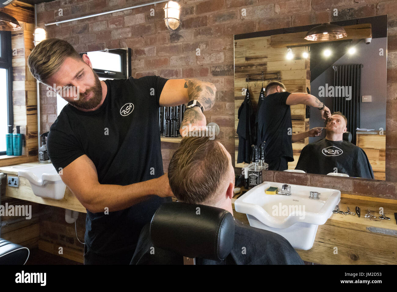 Proprietario Richard Holtham con un cliente al barbiere BS4 in Dudley West Midlands dove ha posato un pavimento contenente circa 70,000 monete 1p ad un costo superiore a £700. Foto Stock