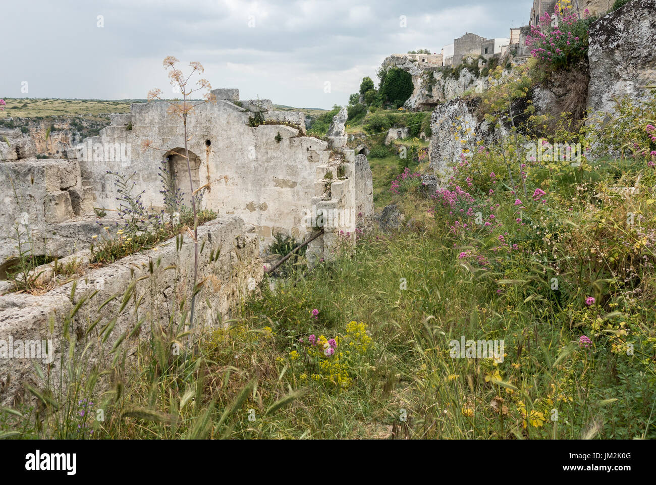 Le rovine della casa in pietra, Matera, Italia. Grotte nella collina di sfondo. Foto Stock