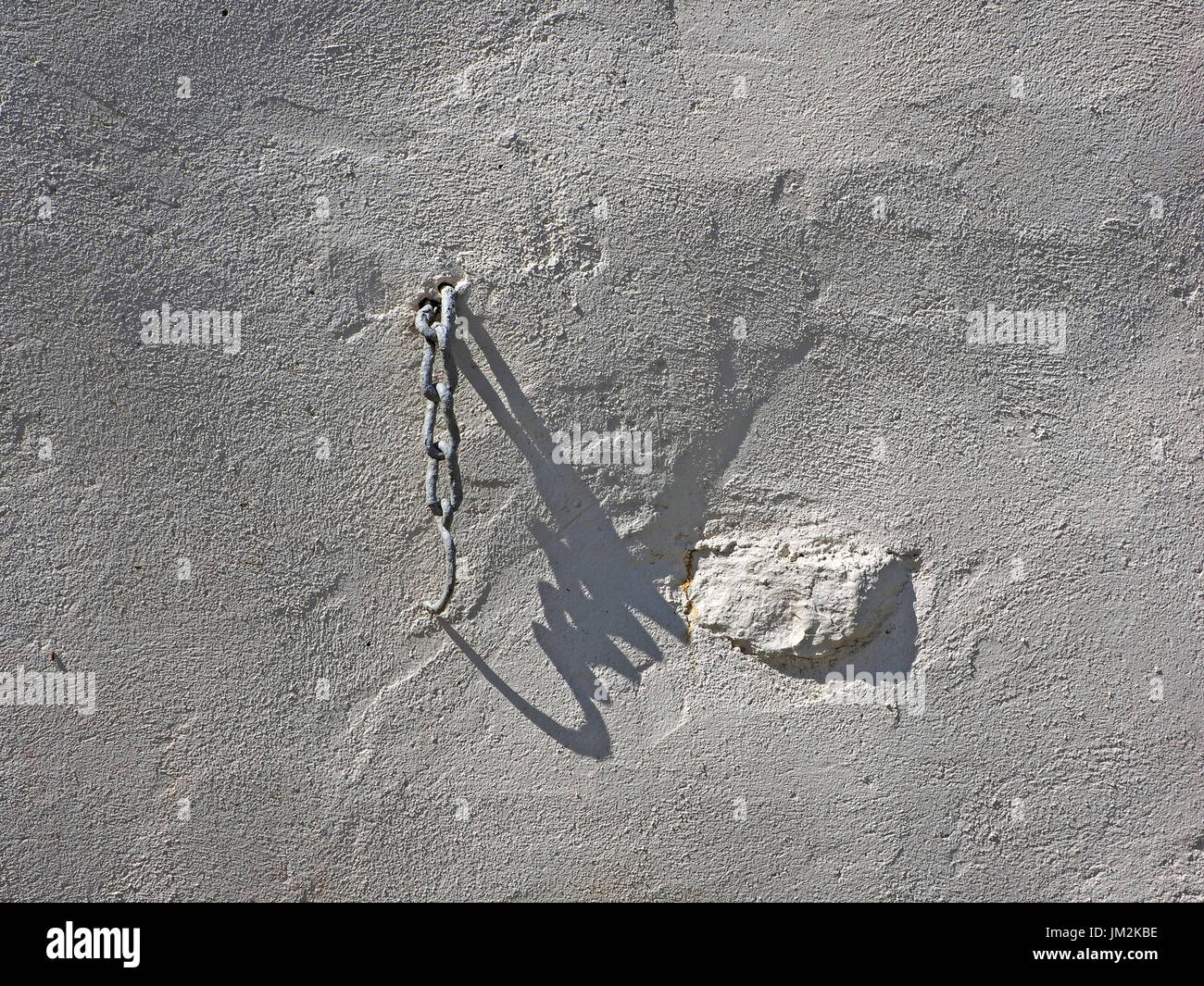 Dipinto di bianco di catena di metallo appeso sul bianco goffrato resi parete drammatico di colata oblique diagonalmente ombra sulla superficie irregolare in Cumbria, England, Regno Unito Foto Stock