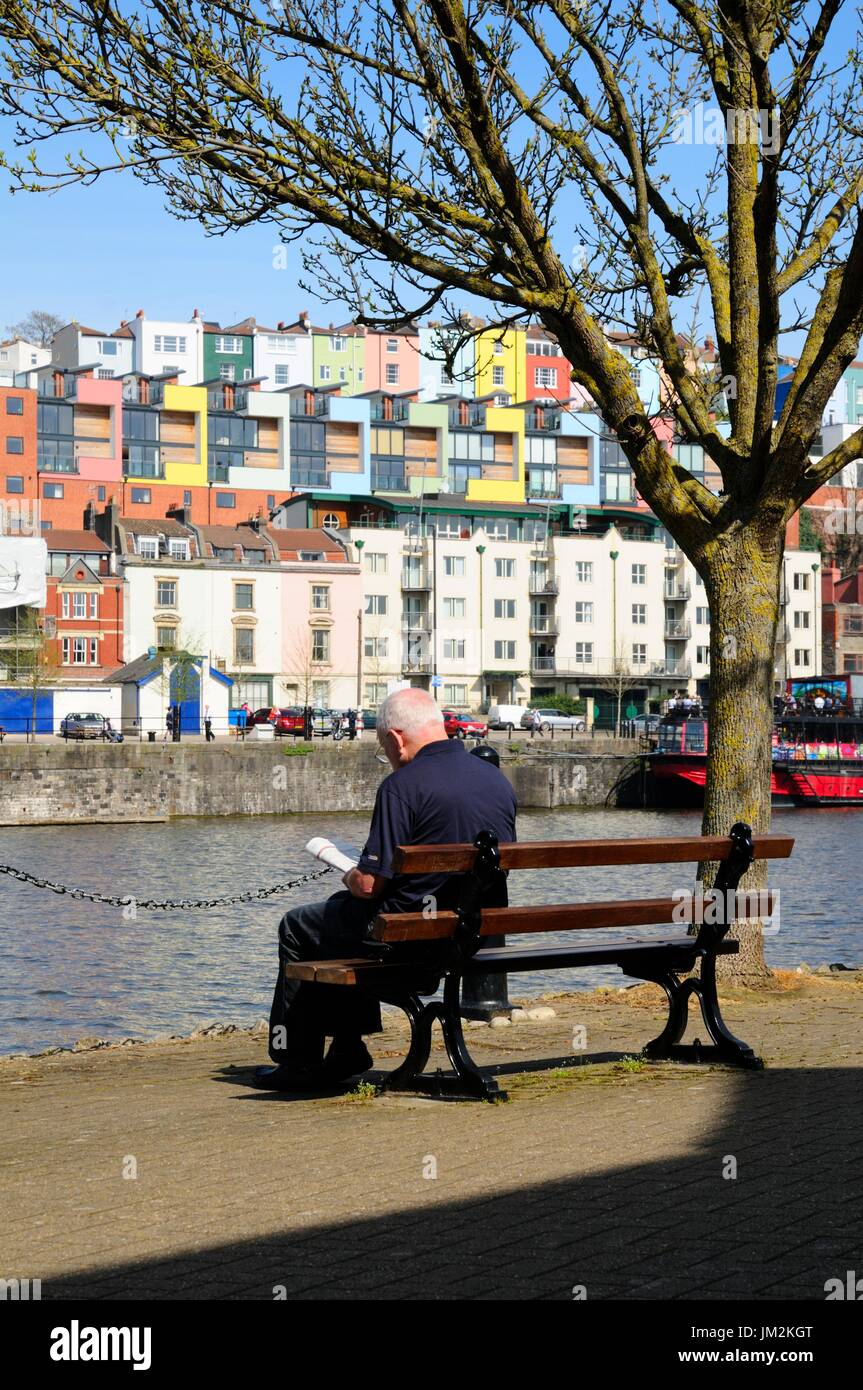 Un Signore più anziano che si gode leggere un libro in piacevole sole sul lungomare di Bristol `s Harbourside. Foto Stock