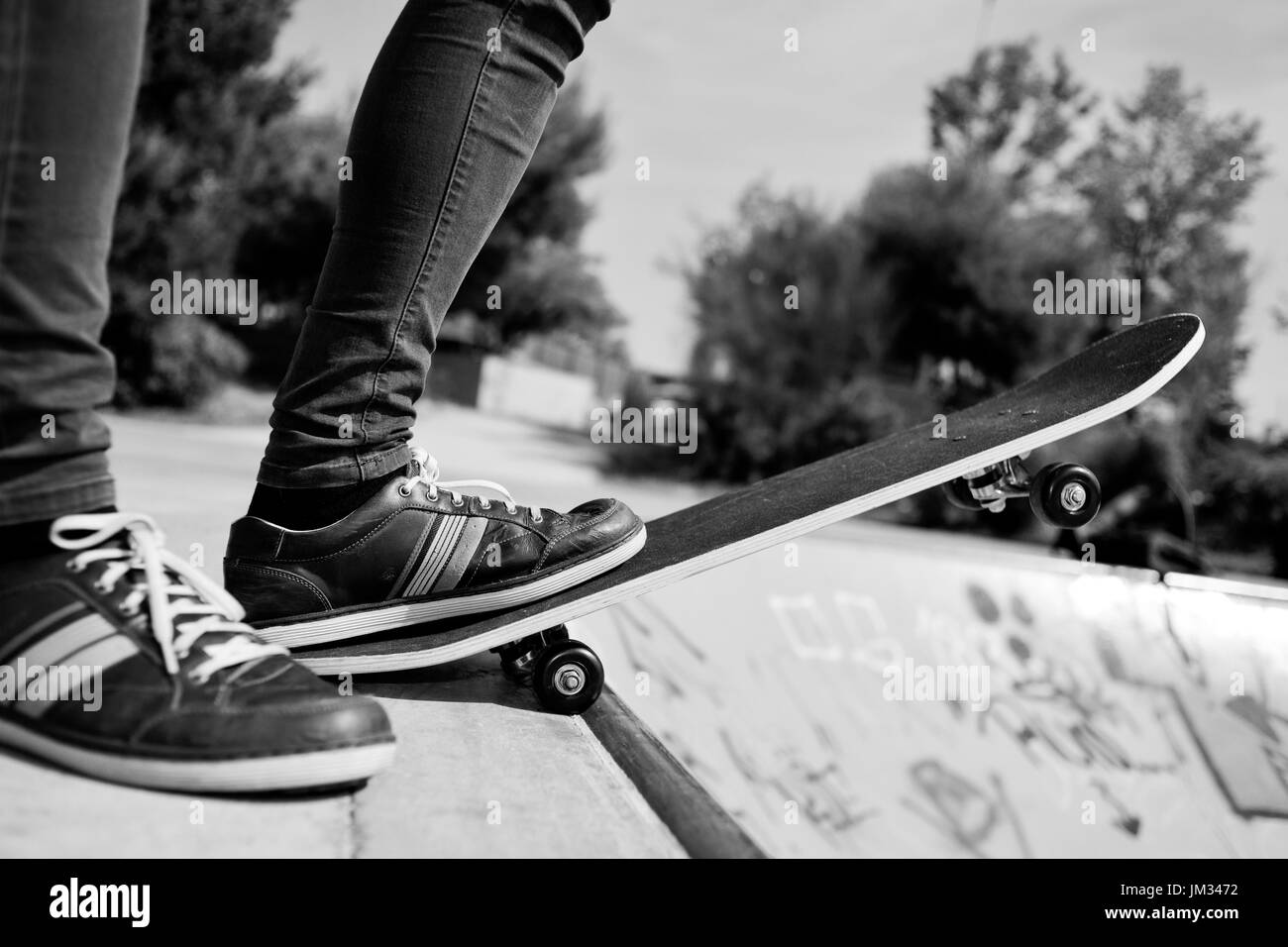 Primo piano di un giovane uomo caucasico skateboarding in un aperto skate park, in bianco e nero Foto Stock