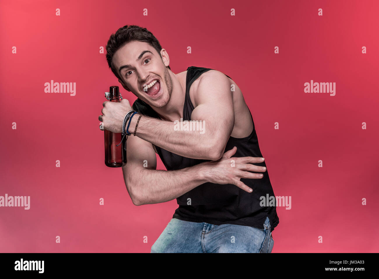 Bel giovane gesticolando con bottiglia di birra e sorridente in telecamera Foto Stock