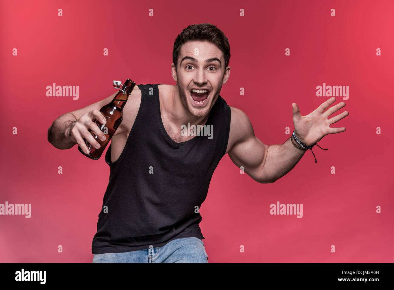 Bel giovane gesticolando con bottiglia di birra e sorridente in telecamera Foto Stock