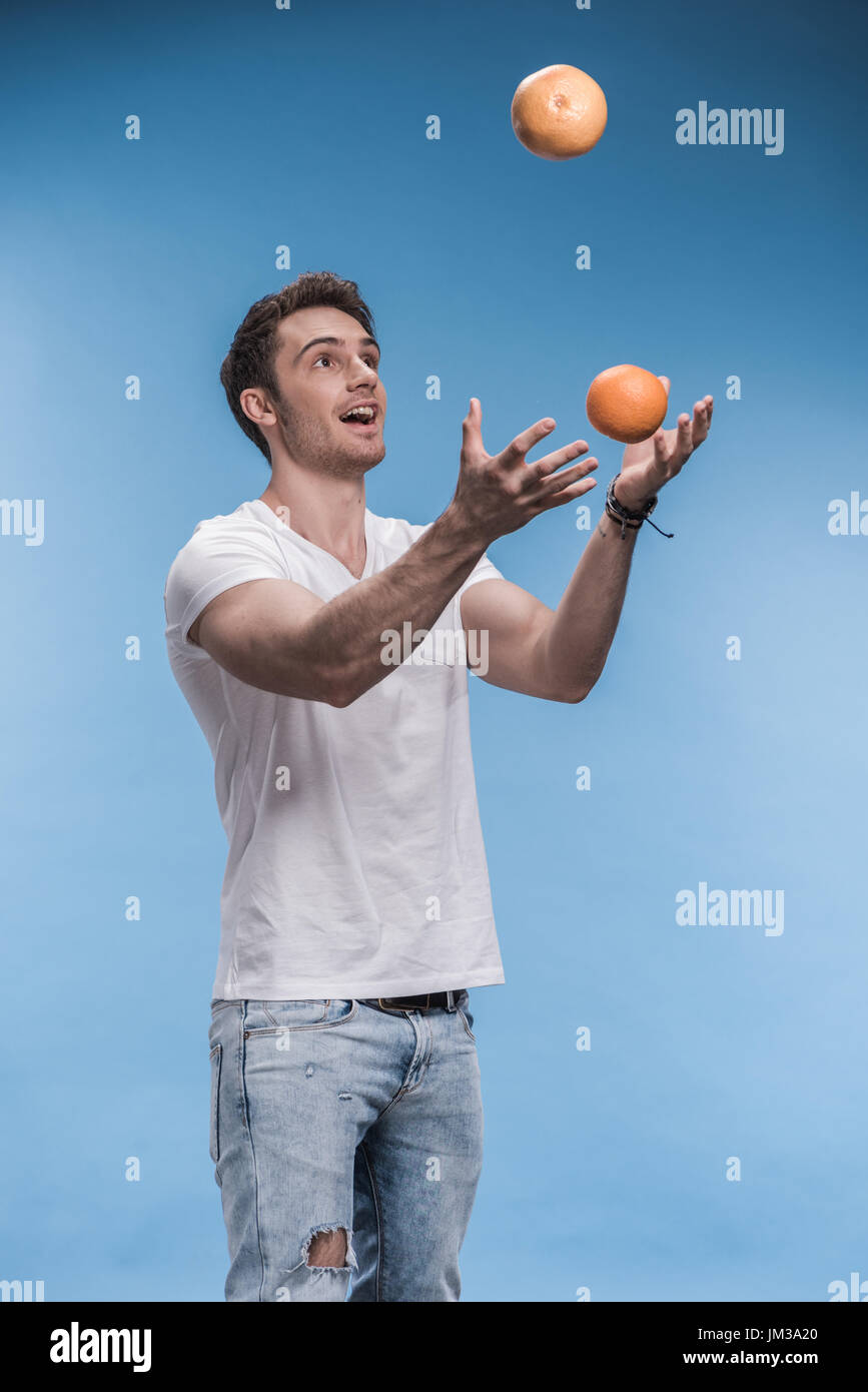 Sorridente giovane giocoleria con frutti isolati su blu Foto Stock