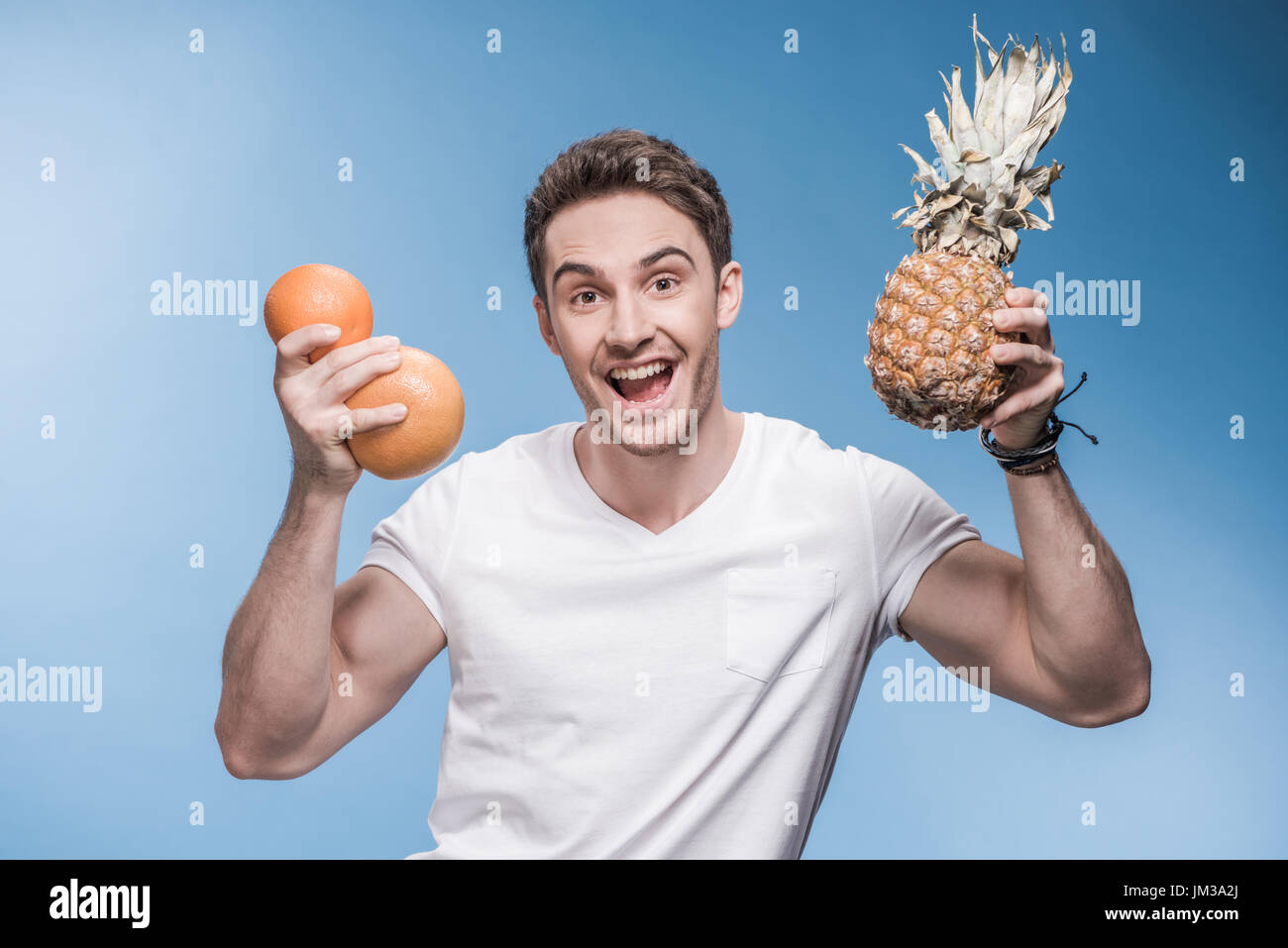 Bel giovane in t-shirt bianco azienda frutta fresca e sorridente in telecamera Foto Stock