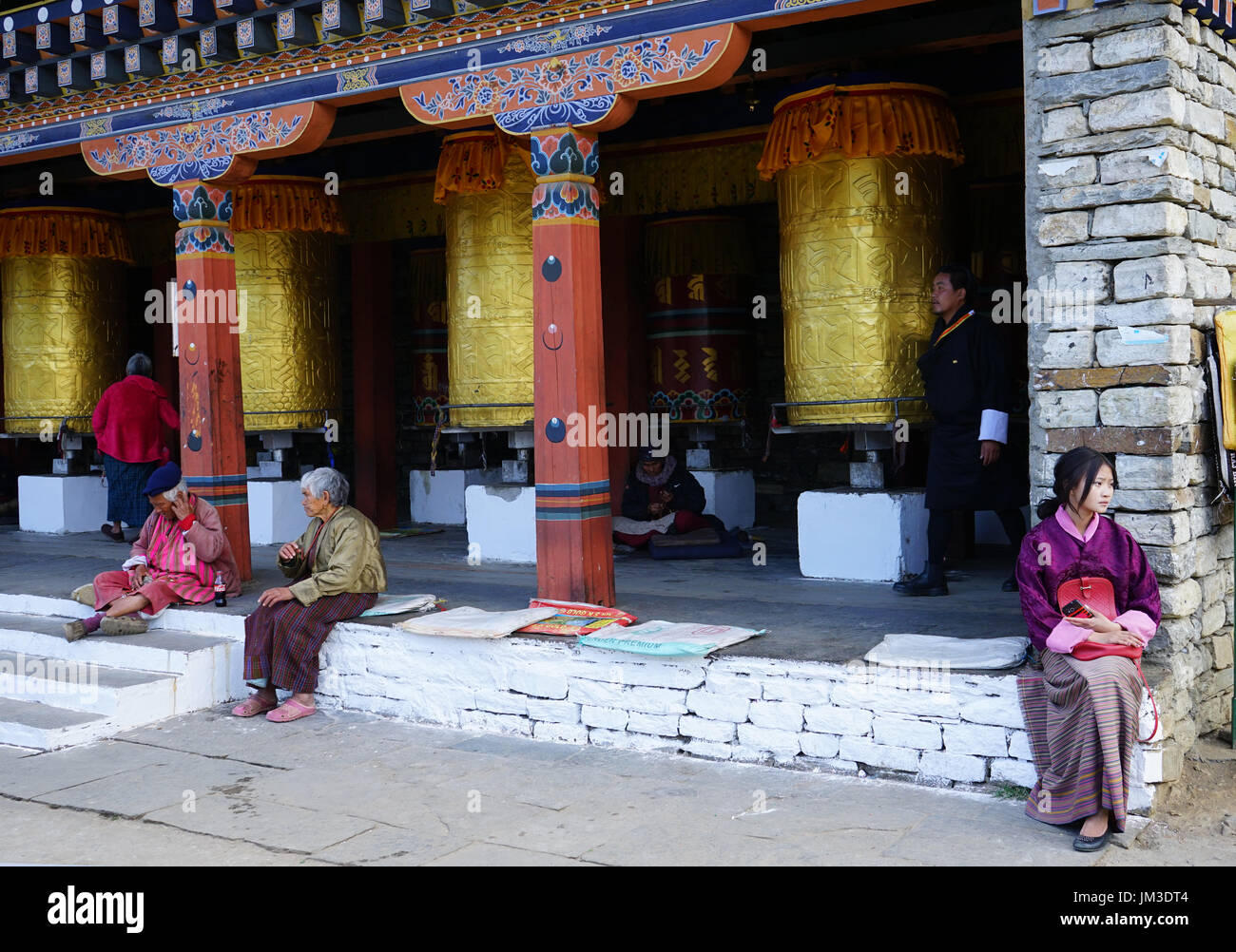 Giovane donna con il cellulare e anziane tradizionalmente condita sitiing presso il Memorial Chorten, Timphu, Bhutan Foto Stock