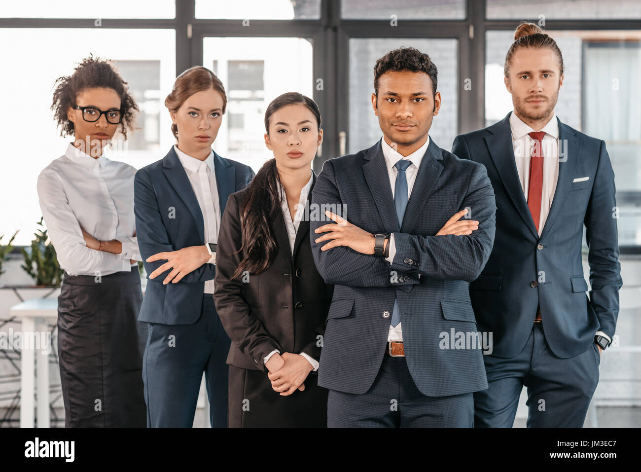 I giovani imprenditori nella convenzionale in posa mentre si sta in piedi in un ufficio moderno e multiculturale di team aziendali Foto Stock