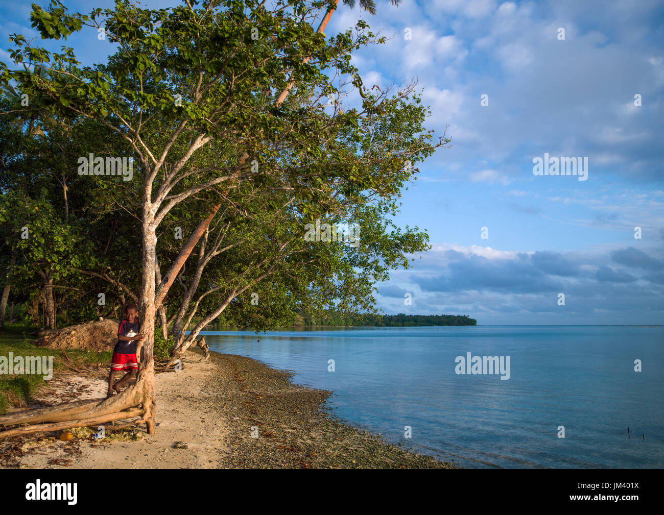 Ragazzo in piedi di fronte a un'acqua turchese e sabbia bianca sulla spiaggia di Erakor, Shefa Provincia, isola di Efate, Vanuatu Foto Stock