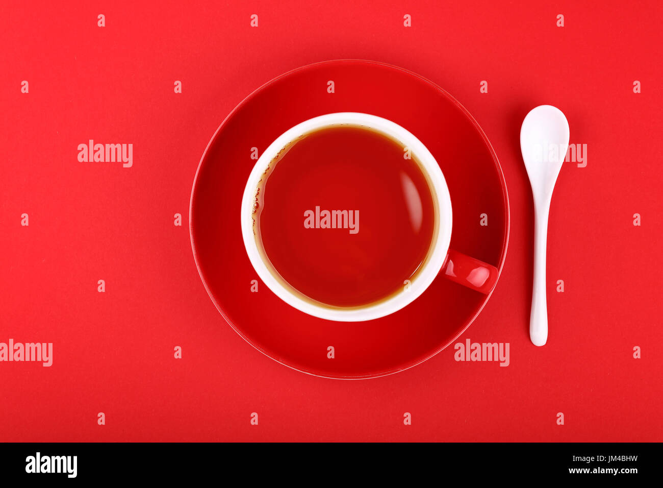 Piena tazza di tè nero su porcellana con piattino in ceramica bianca su cucchiaio rosso vivace sfondo della carta, close up, elevati vista dall'alto, direttamente al di sopra di Foto Stock