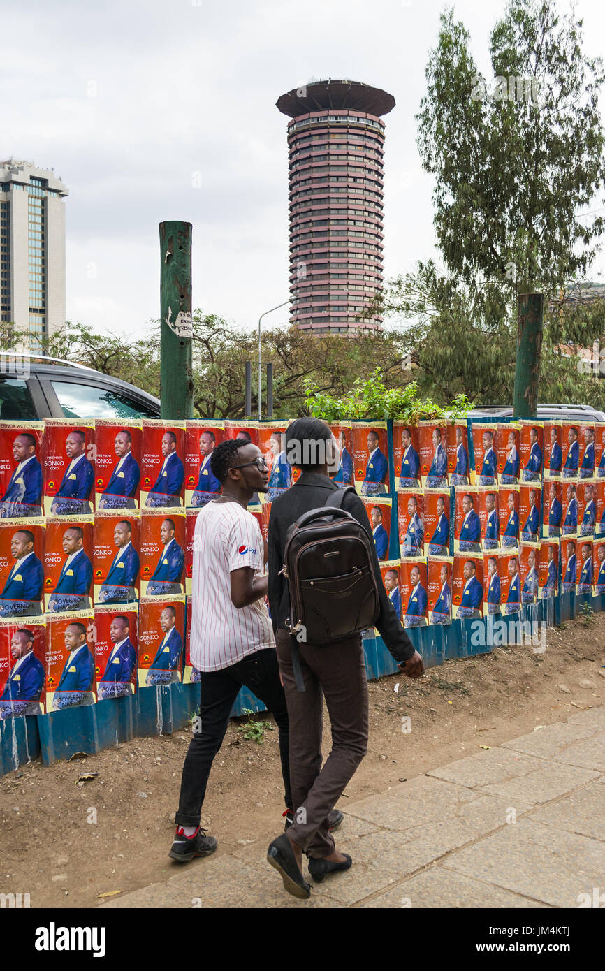 La gente camminare passato keniota candidato alle elezioni poster sulla parete nella città di Nairobi con Kenyatta International Convention Center in background, Kenya Foto Stock