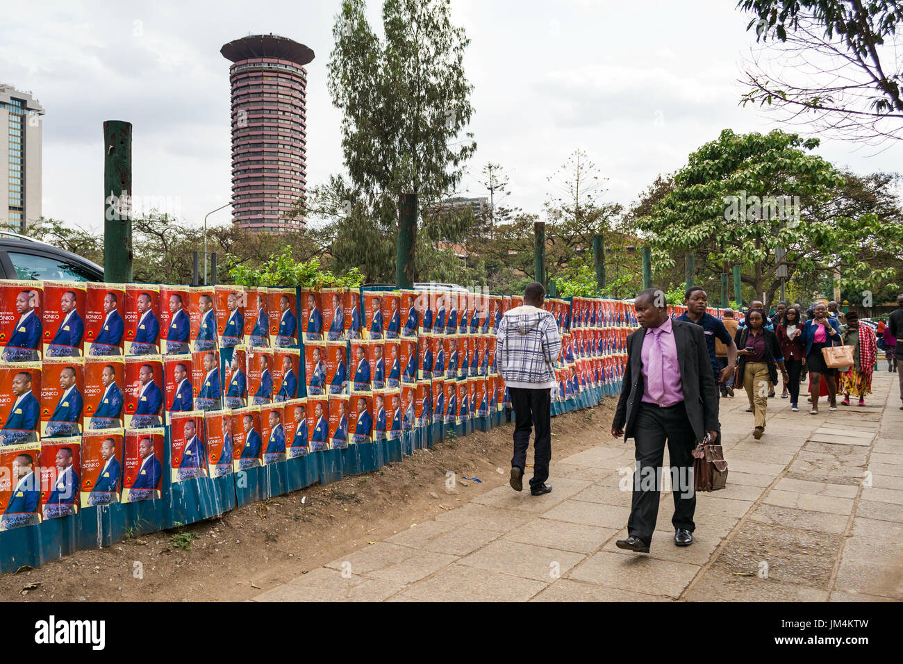 La gente camminare passato keniota candidato alle elezioni poster sulla parete nella città di Nairobi con Kenyatta International Convention Center in background, Kenya Foto Stock