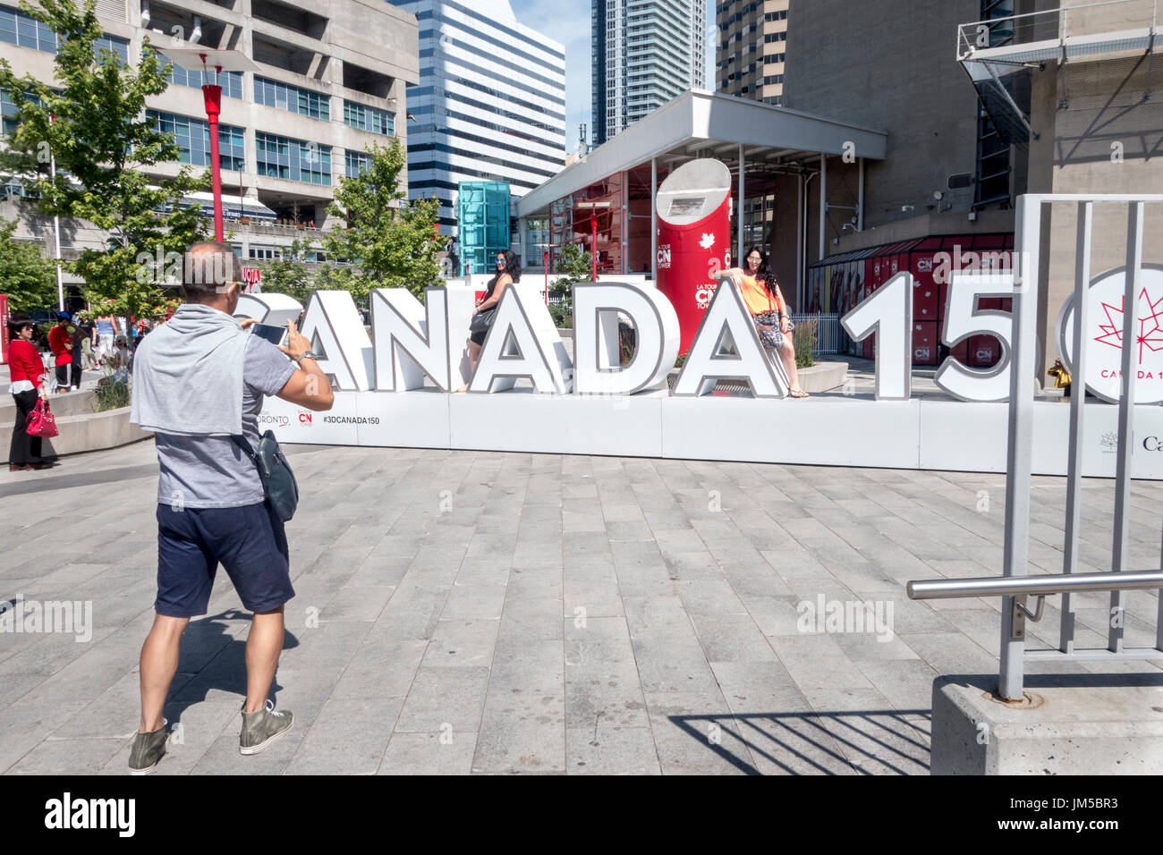 I turisti che pongono al Canada 150 segno esterno della CN tower a Toronto, Ontario, Canada Foto Stock