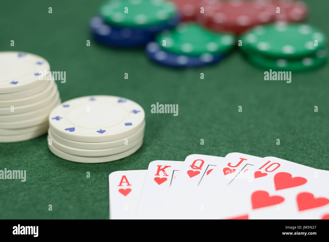 Concetto di gioco in un casinò su una serie vincente giocando a poker con una mano che mostra un royal straight flush sul verde baize con messa a fuoco per una pila di c Foto Stock