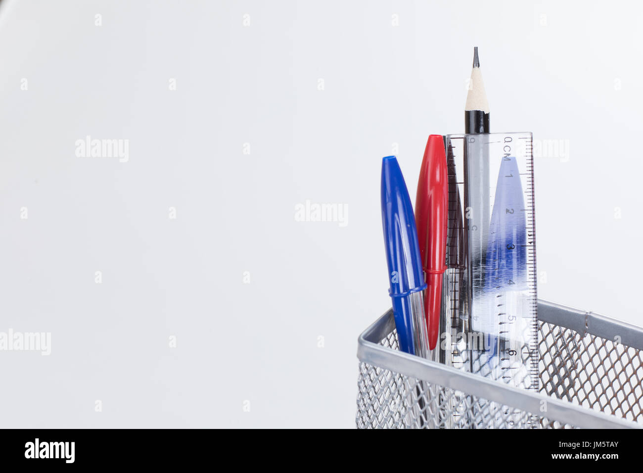 Matite e penne con trasparente righello di plastica in una maglia di filo portapenna isolato su bianco in un concetto di istruzione o di business con spazio copia t Foto Stock