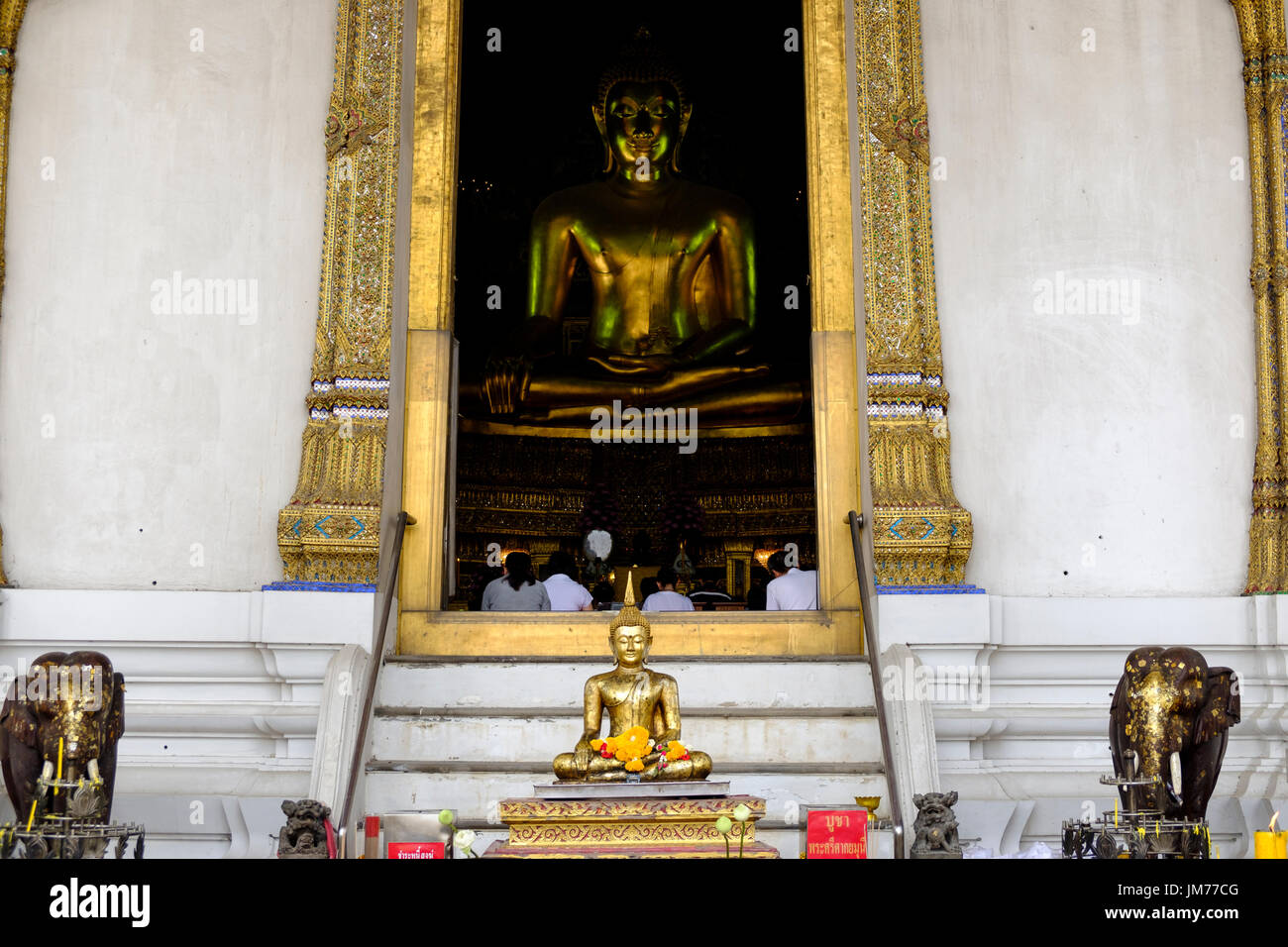 Statua di Buddha e persone in preghiera si vede attraverso l'ingresso A principale sala da preghiera di Wat Suthat Thepwararam, un tempio buddista a Bangkok, in Thailandia. Foto Stock