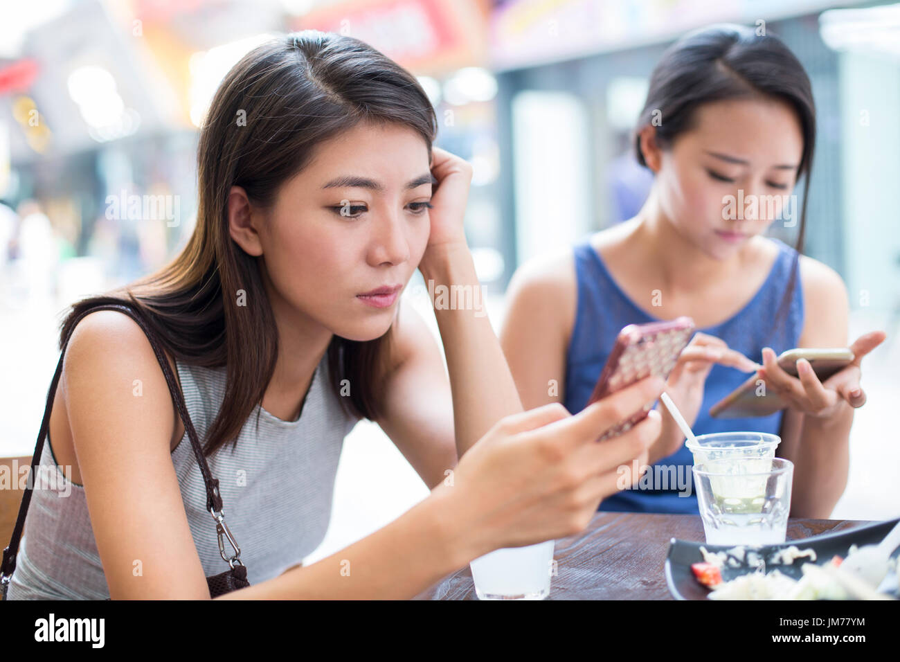 Giovani donne cinesi utilizzando i telefoni intelligenti al marciapiede cafÃ© Foto Stock