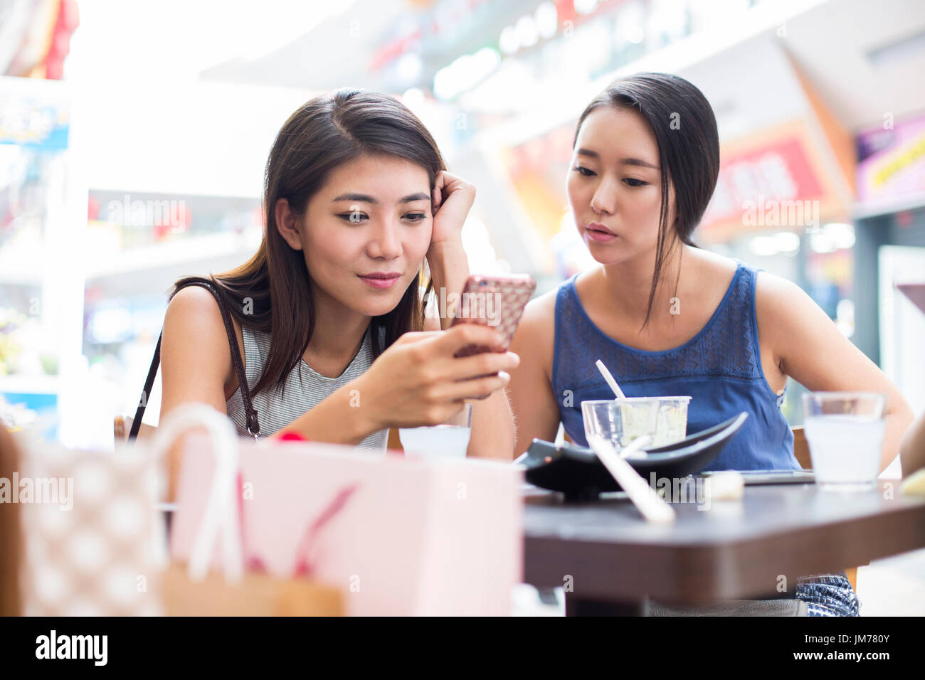 Giovani donne cinesi utilizzando smart phone al marciapiede cafÃ© Foto Stock