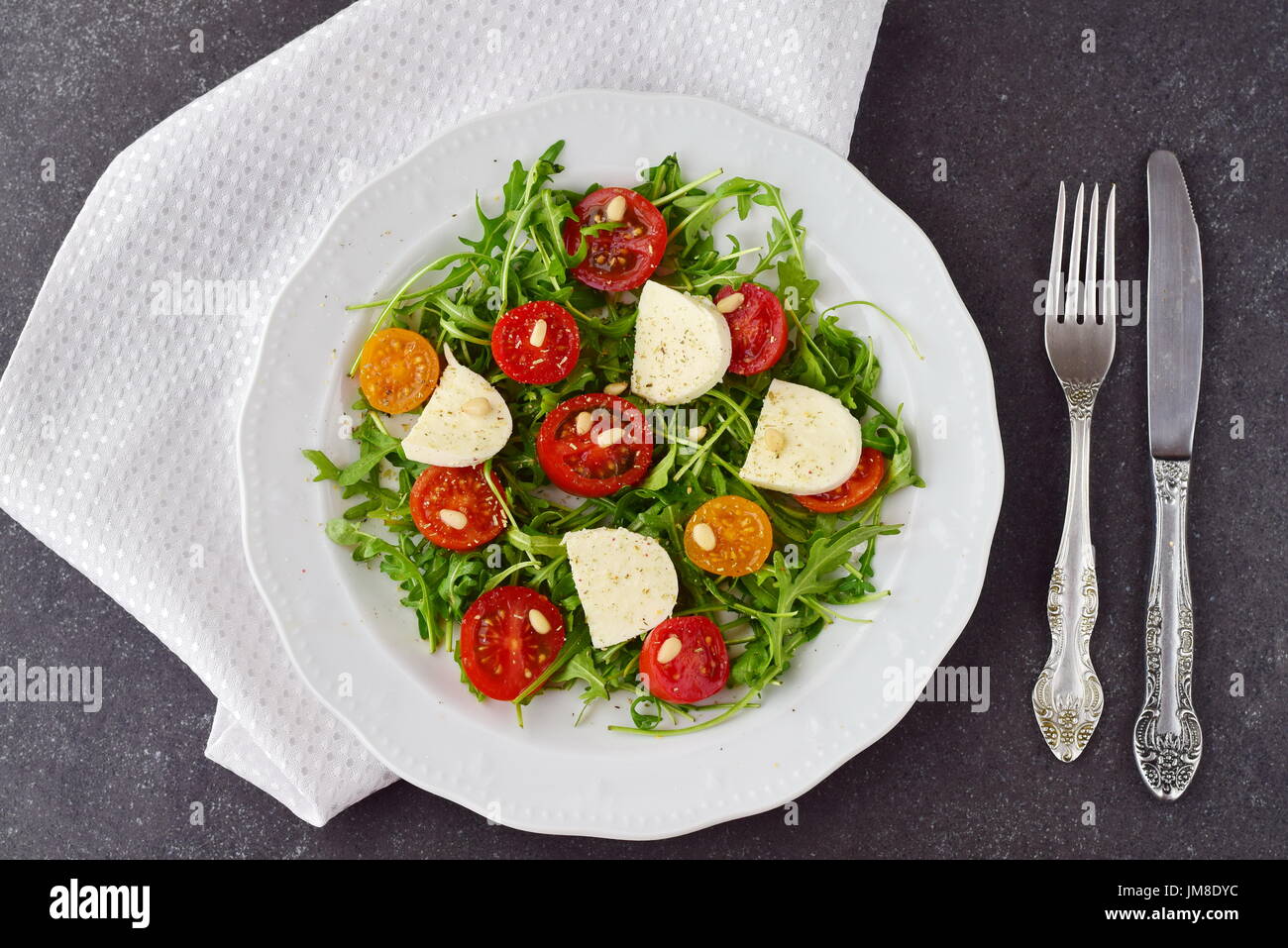 Tradizionale Italiano con insalata di pomodoro ciliegino, rucola, mozzarella, olio di oliva aceto di vino su una piastra bianca su un grigio Sfondo astratto Foto Stock