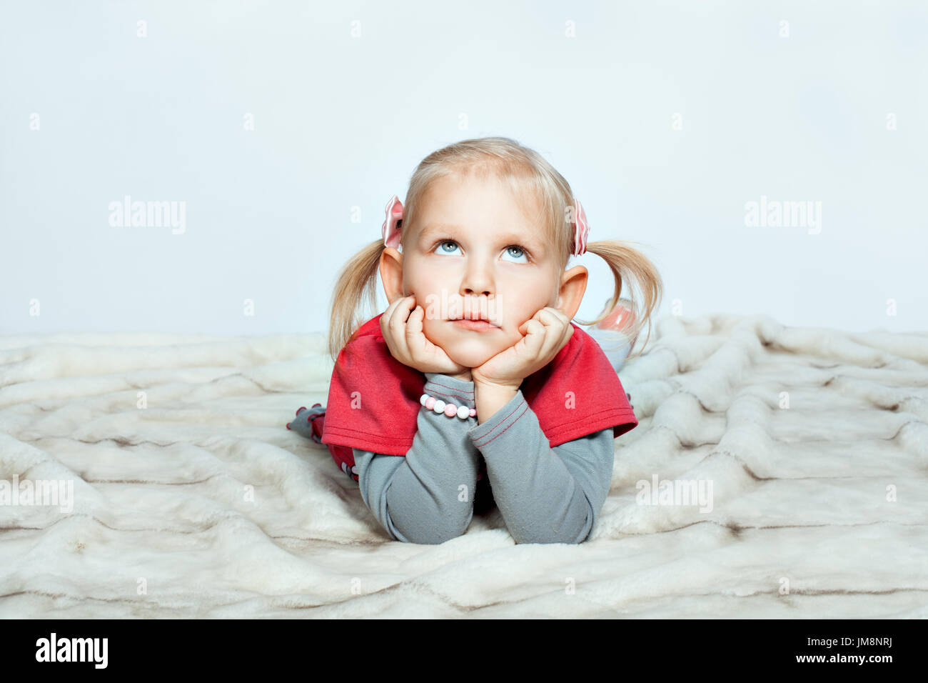 Bellissima bambina è sdraiato con le mani sul suo mento e guardando in alto Foto Stock