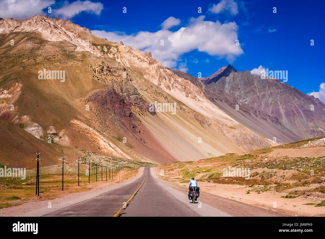 Donna ciclismo su strada vuota da Mendoza in Argentina a Valparaiso in Cile, arrampicata costantemente al confine e passaggio di Parco Nazionale Aconcagu Foto Stock