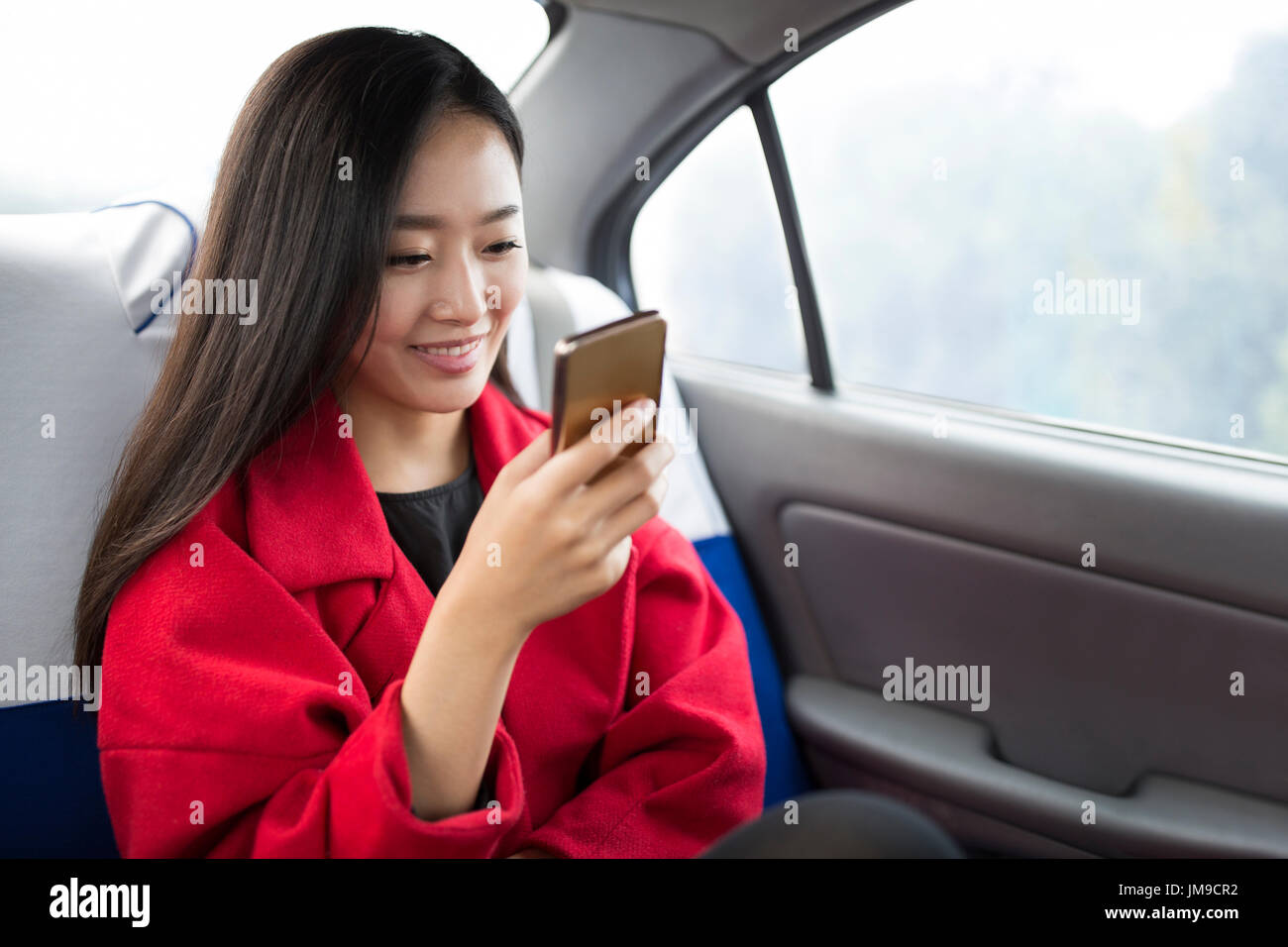 Il cinese giovane donna utilizzando smart phone all'interno dell'auto Foto Stock