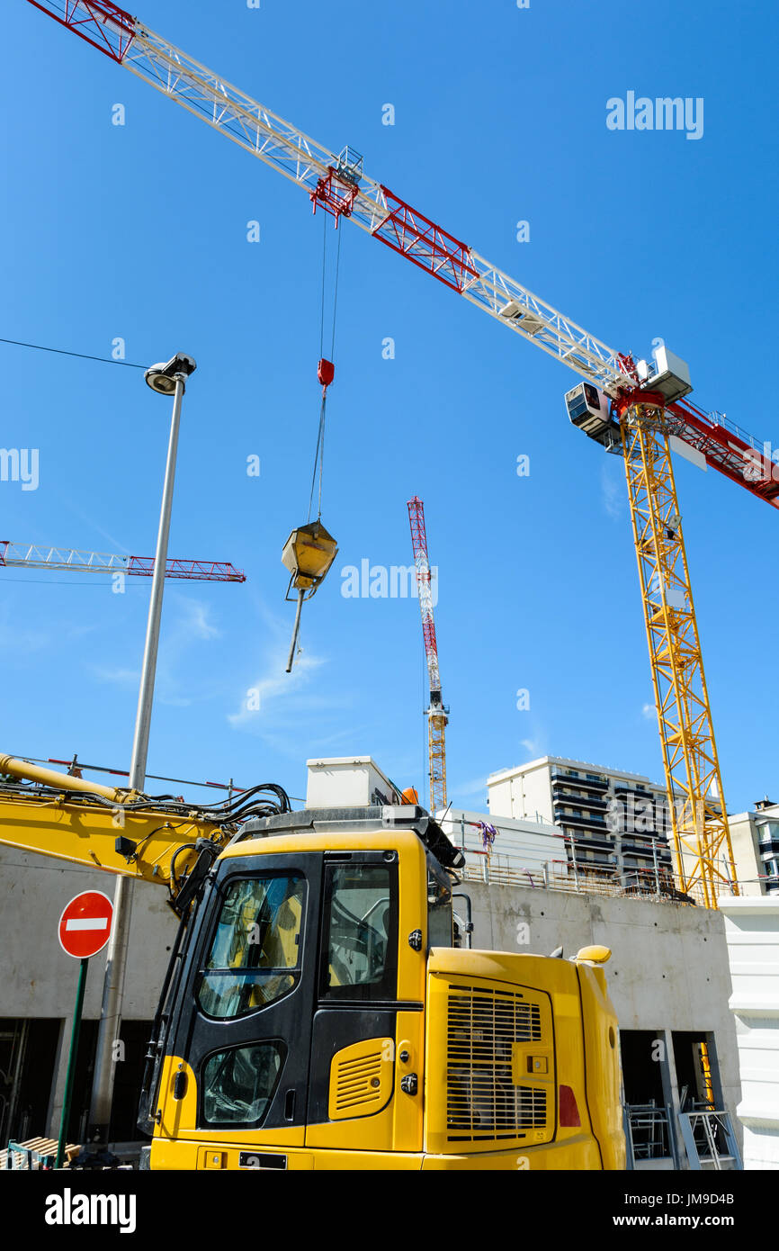 Basso angolo vista di gru a torre in un cantiere con escavatore giallo in primo piano. Foto Stock