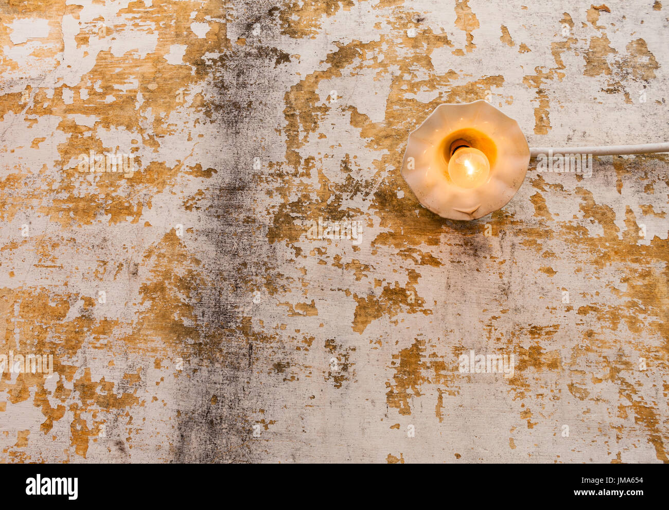 Una luminosa accesa lampada ad incandescenza con filamento giallo su una vecchia parete scheggiata. Foto Stock