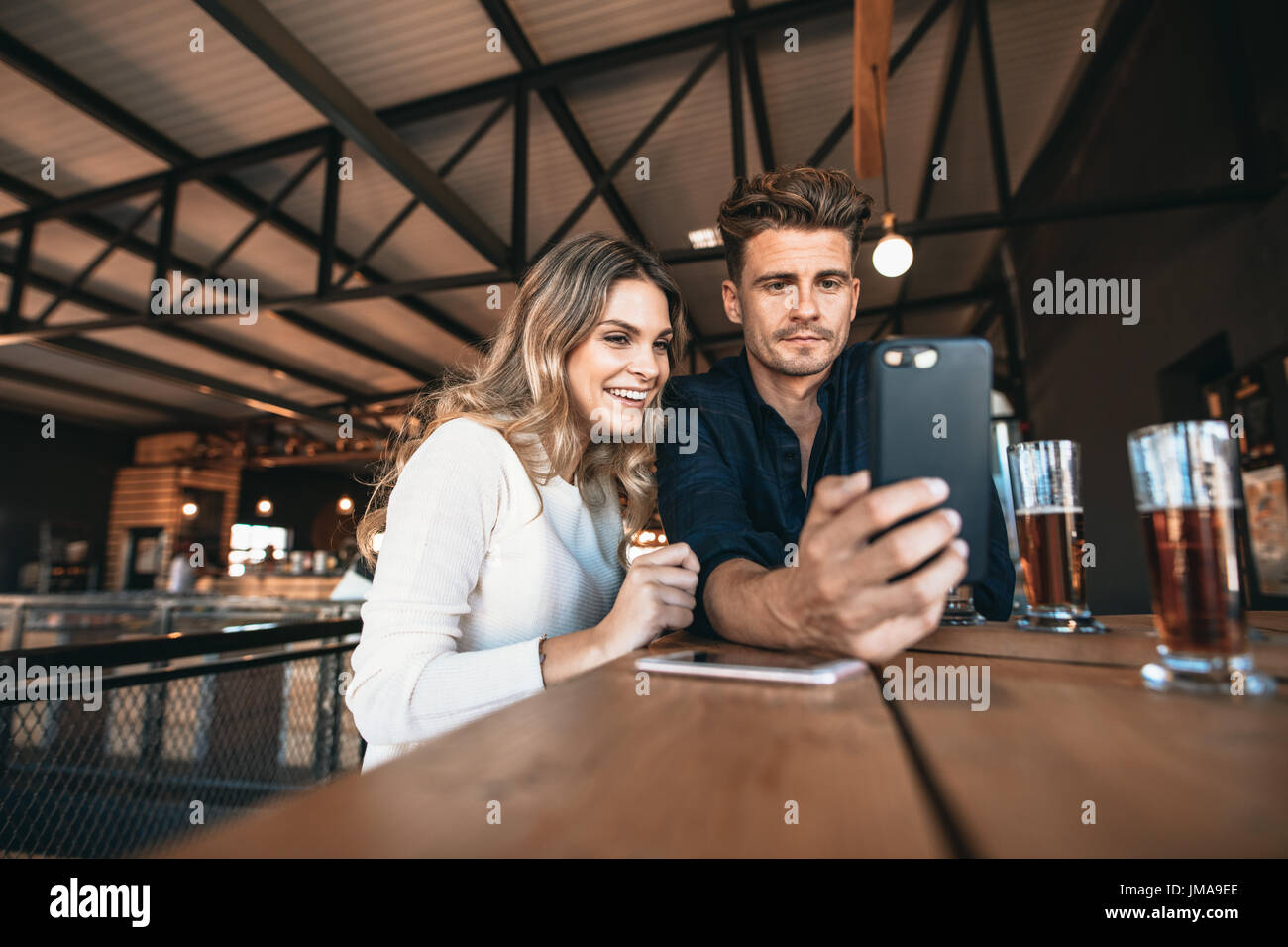 Coppia giovane al bar tenendo selfie con il telefono cellulare. Focus su smart phone in mano dell'uomo. Foto Stock