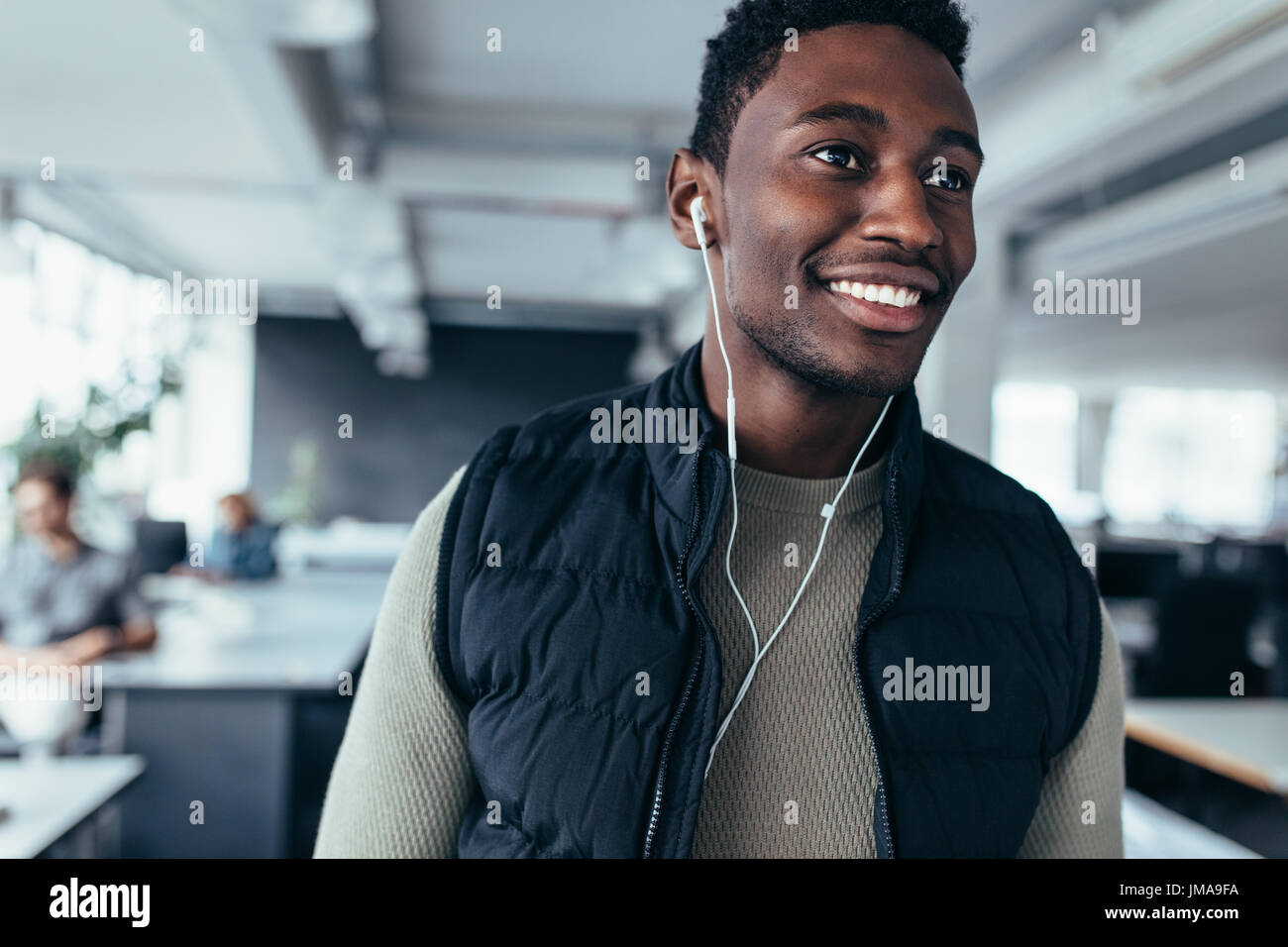 Executive maschio ascoltando la musica con gli auricolari mentre in piedi in ufficio. African giovane uomo che ascolta musica in ufficio di progettazione. Foto Stock