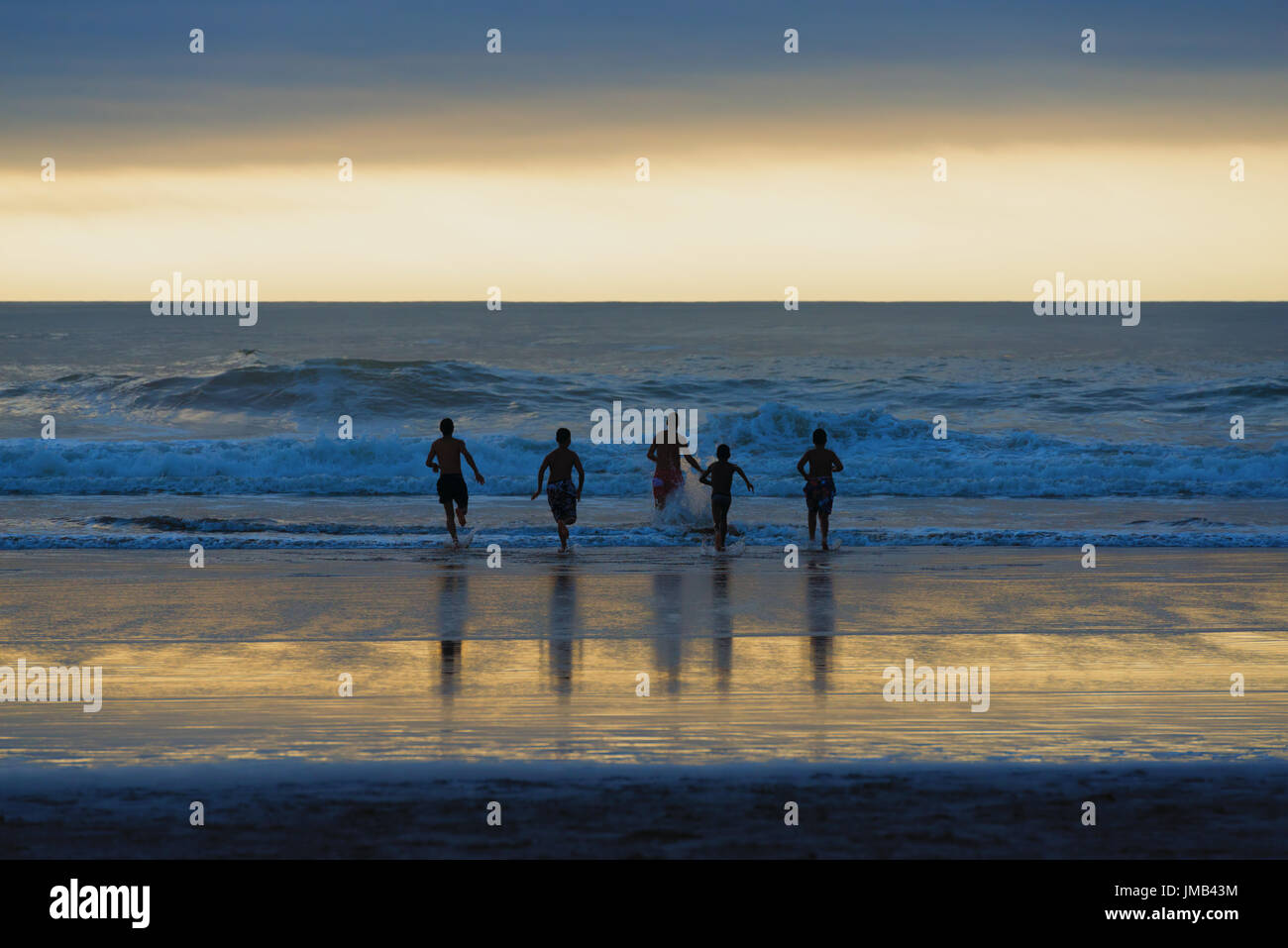 Silhouette di quattro giovani uomini (ragazzi) in spiaggia in esecuzione nel surf. Foto Stock