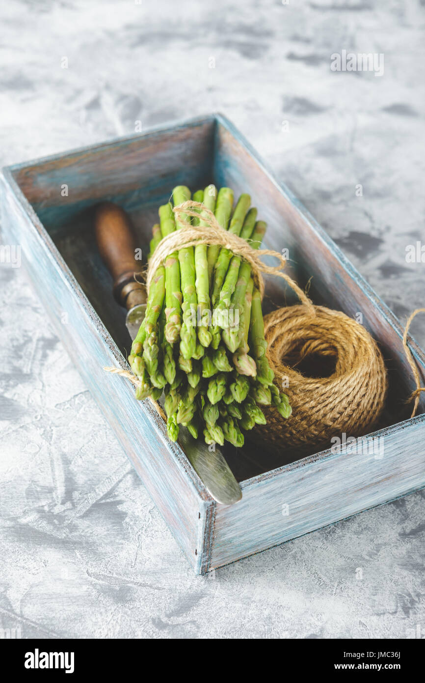 Materie di asparagi, groviglio di corda e coltello in una scatola di legno su sfondo chiaro Foto Stock