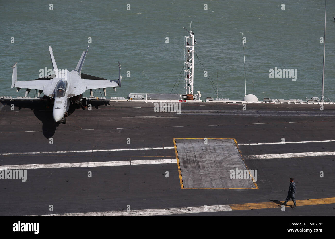 Membro dell'equipaggio passeggiate lungo il flightdeck vicino a un F-18 jet da combattimento a bordo della US Navy Nimitz-class portaerei USS George H.W. Bush come si stabilisce al di ancoraggio fuori coastbefore partecipa n esercizio guerriero sassone 2017 nel Nord dell'Oceano Atlantico. Foto Stock
