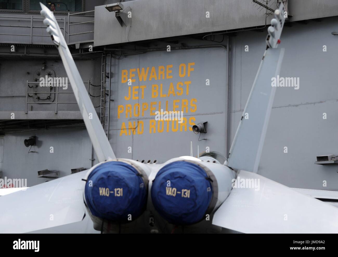 Un F-18 si siede di fronte a un cartello attenzione del Jet Blast Eliche e rotori a bordo della US Navy Nimitz-class portaerei USS George H.W. Bush come si stabilisce al di ancoraggio al largo prima di esso partecipa in esercizio guerriero sassone 2017 nel Nord dell'Oceano Atlantico. Foto Stock