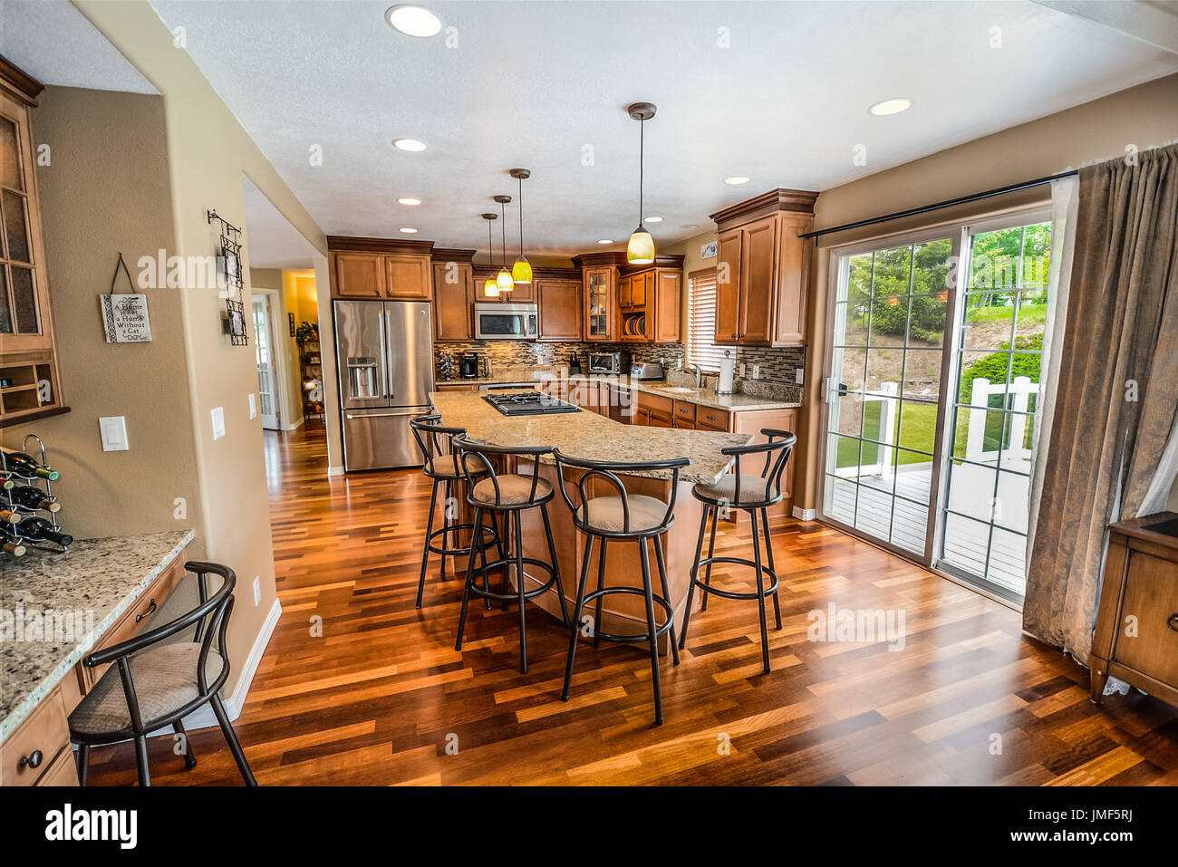 Elegante e spaziosa cucina di lusso con granito di grandi dimensioni in alto al centro isola e gli elettrodomestici in acciaio inox e cursore a un patio aperto Foto Stock