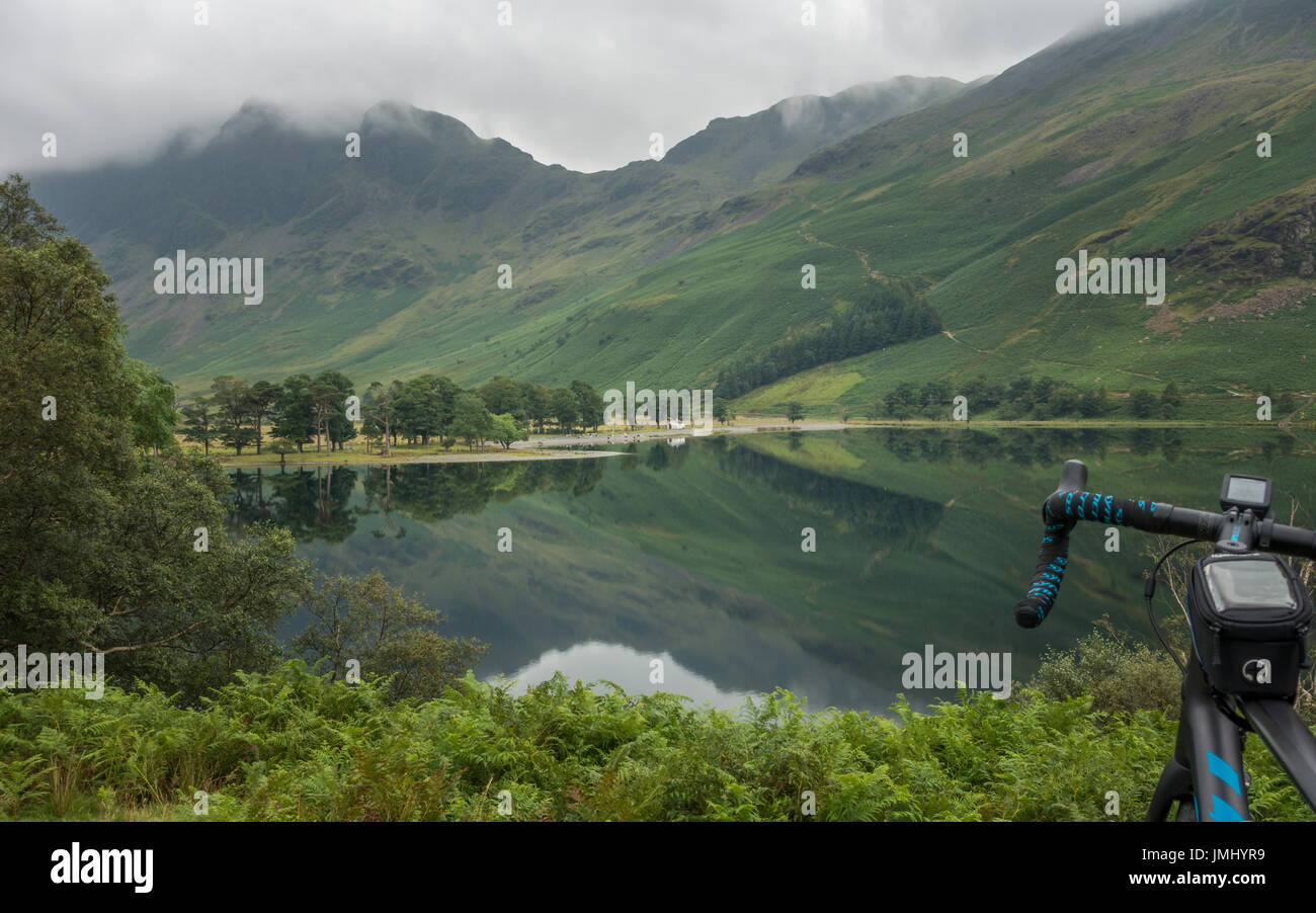 Regno Unito uno scenario paesaggistico: ciclista sosta per scattare foto a Buttermere. Ancora un giorno con il percorso di Scarth gap in background, Lake District inglese Foto Stock