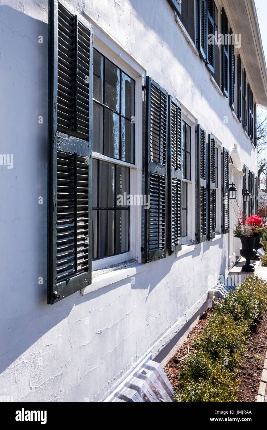 Guardando verso il basso il soleggiato esterno di un bianco edificio dipinto di nero otturatori fiancheggianti il windows. Foto Stock